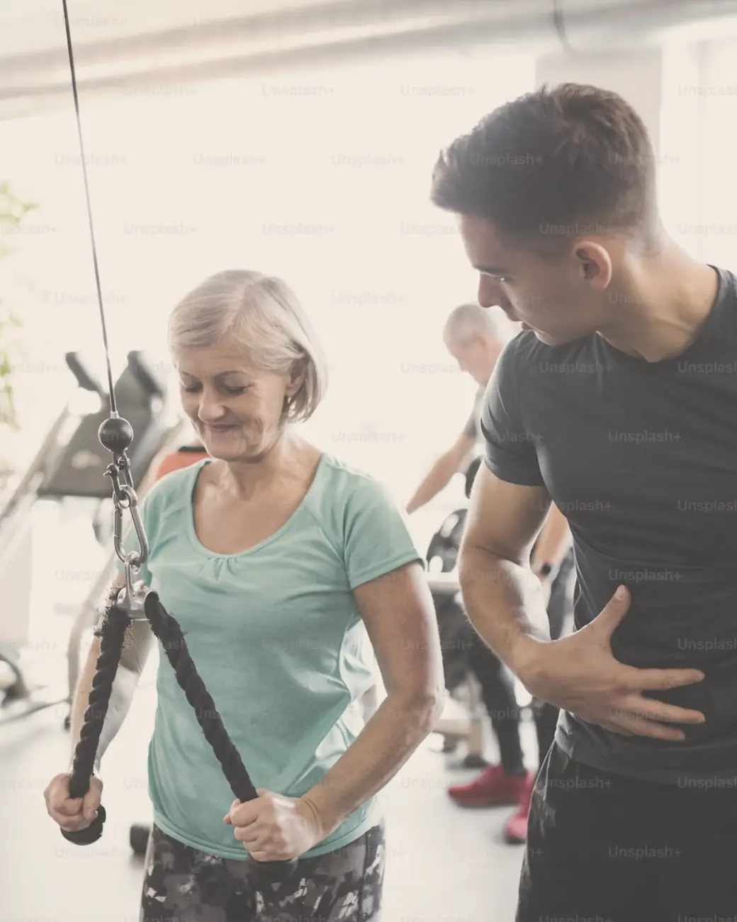 A trainer coaching an older client through a cable exercise